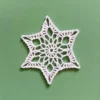 Gwiazdka na choinkę zrobiona na szydełku z białego kordonka, na zielonym tle