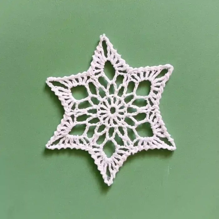 Gwiazdka na choinkę zrobiona na szydełku z białego kordonka, na zielonym tle