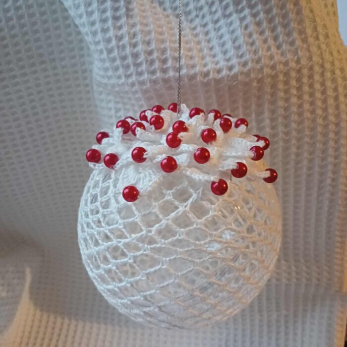 Duża bombka dekoracyjna zrobiona szydełkiem z białego kordonka, wzór z kwiatem z czerwonymi perełkami.