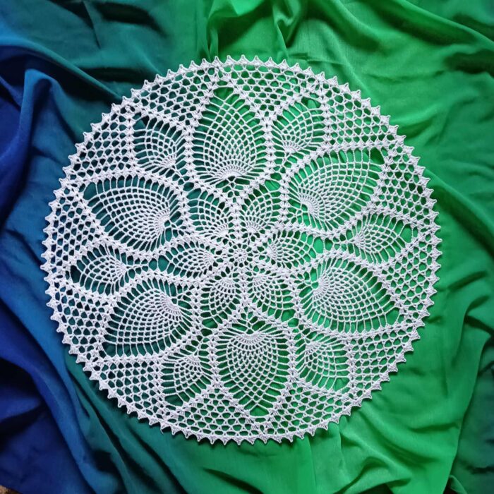 Serweta zrobiona ręcznie na szydełku- mandala z białego kordonka, wykonana wzorem w ananaski rozłozona na zielonogranatowym materiale