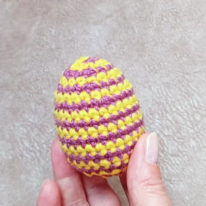 W dłoni Jajko z włóczki zrobione na szydełku wzorem w wąskie paseczki