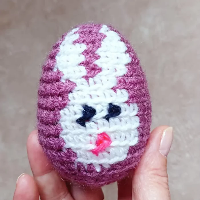W dłoni Jajko z włóczki zrobione na szydełku wzorem z obrazkiem królika
