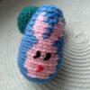 Jajko z niebieskiej włóczki zrobione na szydełku z obrazkiem głowy królika w kolorze różowym leżące na podkładce.