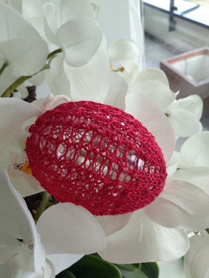 Jajko leżące na białych kwiatach ubrane w czerwoną koszulkę zrobioną na drutach