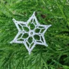 Gwiazdka na choinkę zrobiona na szydełku z białego kordonka leżąca na zielonym krzewie
