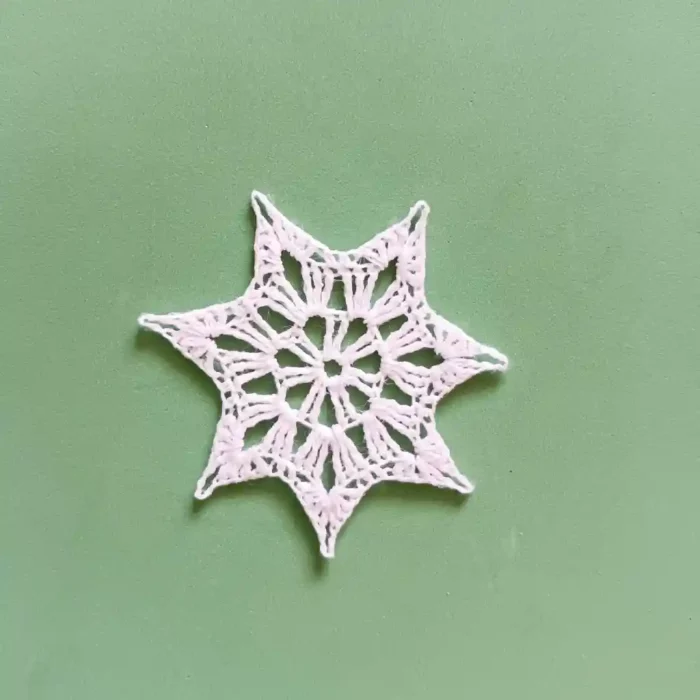 Gwiazdka na choinkę zrobiona na szydełku z białego kordonka, na zielonym tle.