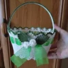 Koszyczek wielkanocny zrobiony na szydełku z białego kordonka z zielonym wykończeniem brzegów koszyczka i raczki, ozdobiony zieloną wstążką i białymi różyczkami