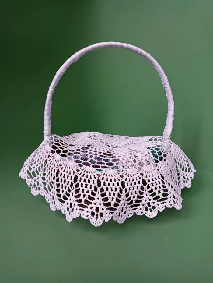 Jaka serwetka do koszyczka? Serwetka do koszyczka z przerwami na pałączek prezentowana na koszyczku, na zielonym tle.