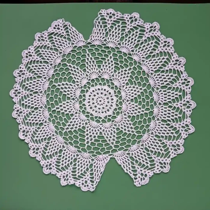 Szydełkowa serwetka do koszyczka wielkanocnego z przerwami po bokach na pałączek koszyczka, zrobiona z białego kordonka, prezentowana na zielonym tle