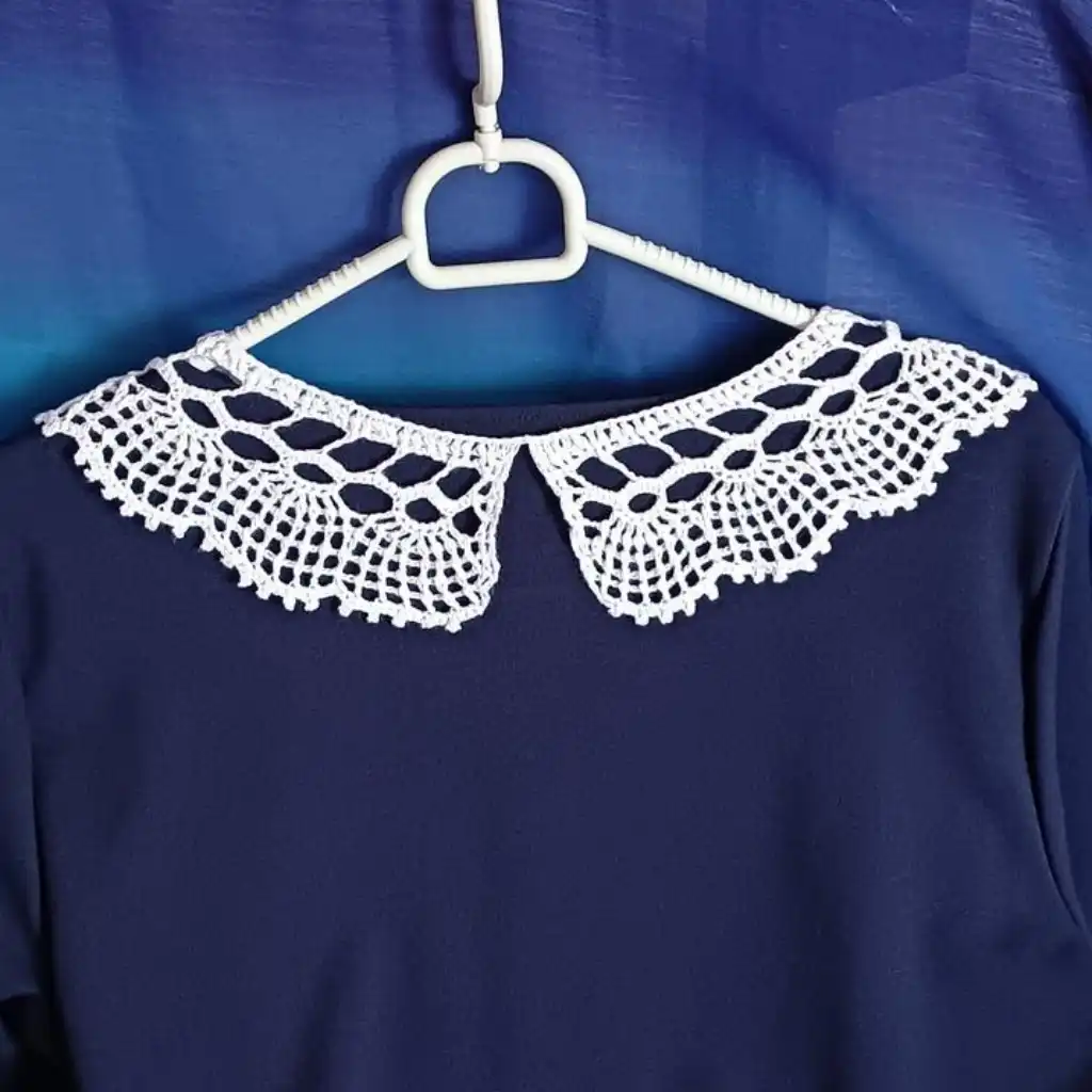 Kołnierzyk dwuczęściowy 3D zrobiony na szydełku z białego kordonka prezentowany na granatowej sukience na wieszaku
