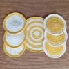 Dwukolorowe, kremowo-żółte, okrągłe podkładki ochronne na stół zrobione na szydełku. 6 mniejszych i 1 większa.