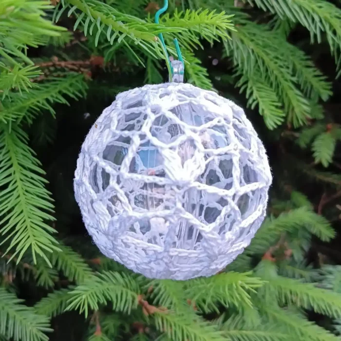 Bombka choinkowa zrobiona na szydełku zawieszona na zielonej swierkowej gałązce