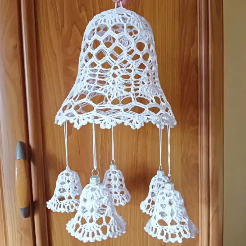 Zdjęcie przedstawia ozdobę świąteczną. Jest to duży dzwonek, do którego doczepionych jest 5 małych dzwoneczkow zrobionych na szydelku.