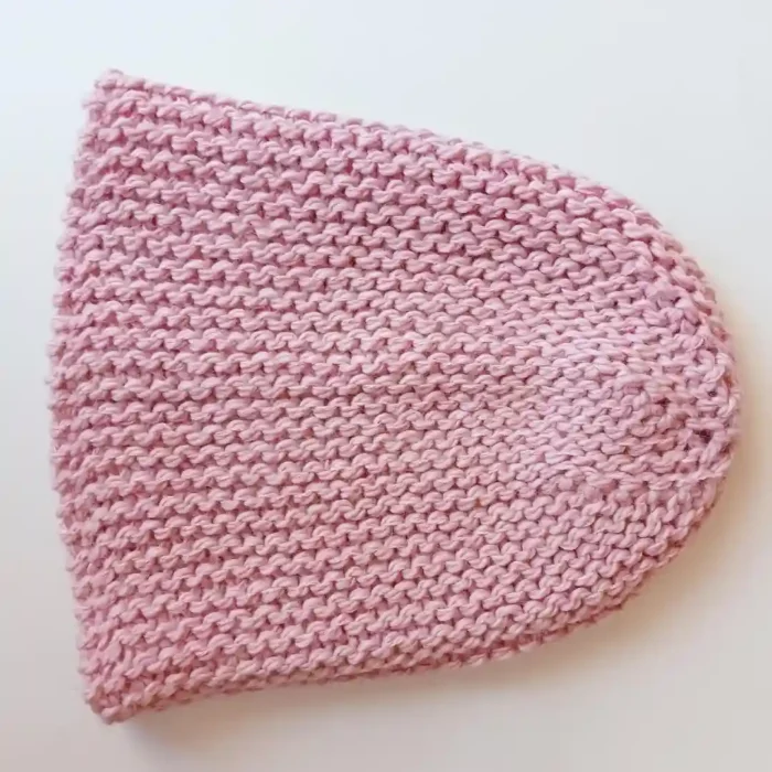 Ciepła czapka na zimę w kolorze pastelowego różu rozłożona na płasko na białym podłożu.