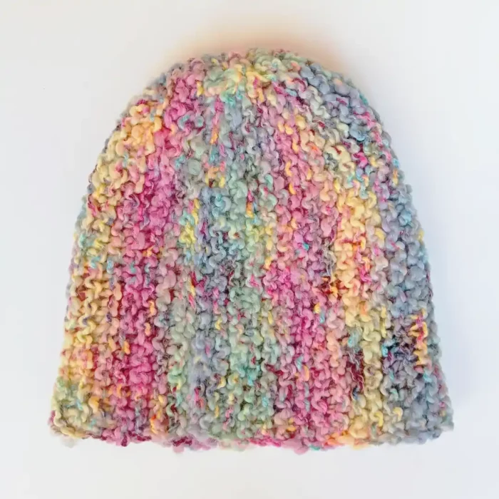 Czapka damska z fantazyjnej włóczki położona na płasko na białym tle