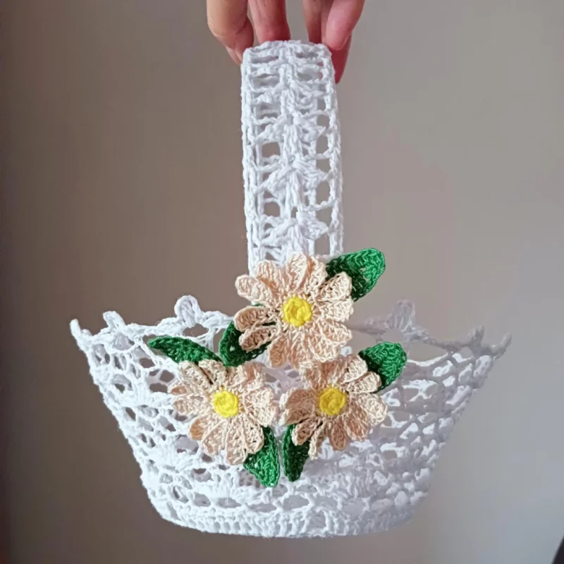 Szydełkowy koszyczek z ozdobnymi stokrotkami Dłoń trzymająca szydełkowy koszyczek z ozdobnymi stokrotkami na beżowym tle