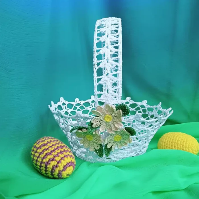 Szydełkowy koszyczek z ozdobnymi stokrotkami na tle zielonego materiału