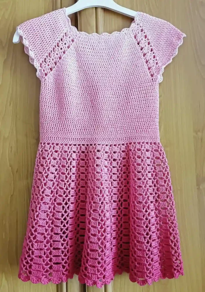 Szydełkowa różowa sukienka dla dziewczynki zawieszona na wieszaku