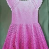 Szydełkowa różowa sukienka dla dziewczynki rozłożona na zielonym materiale