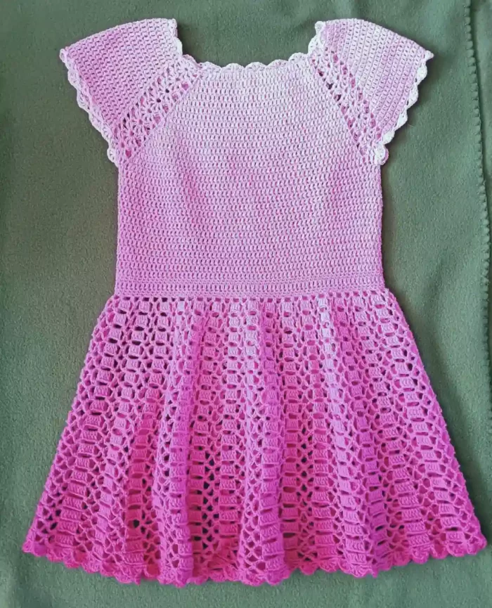 Szydełkowa różowa sukienka dla dziewczynki rozłożona na zielonym materiale
