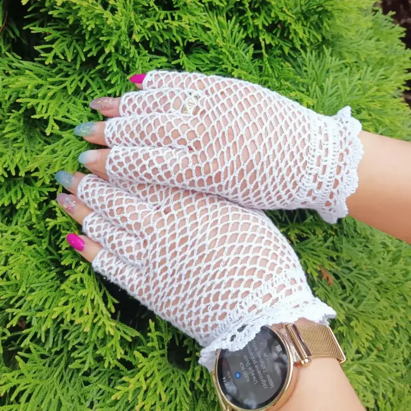 Rękawiczki szydełkowe siateczkowe w rozmiarze S-M_12 Dłonie w białych szydełkowych rękawiczkach zrobionych na szydełku wzorem siateczkowym, bez zakończeń palców.