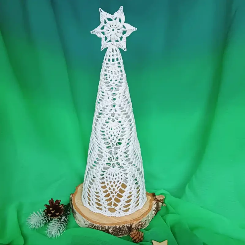 Choinka 3D w ananaski zrobiona na szydełku z białego kordonka, utwardzona klejem, stojąca na drewnianej podstawie, z gwiazdką na czubku.