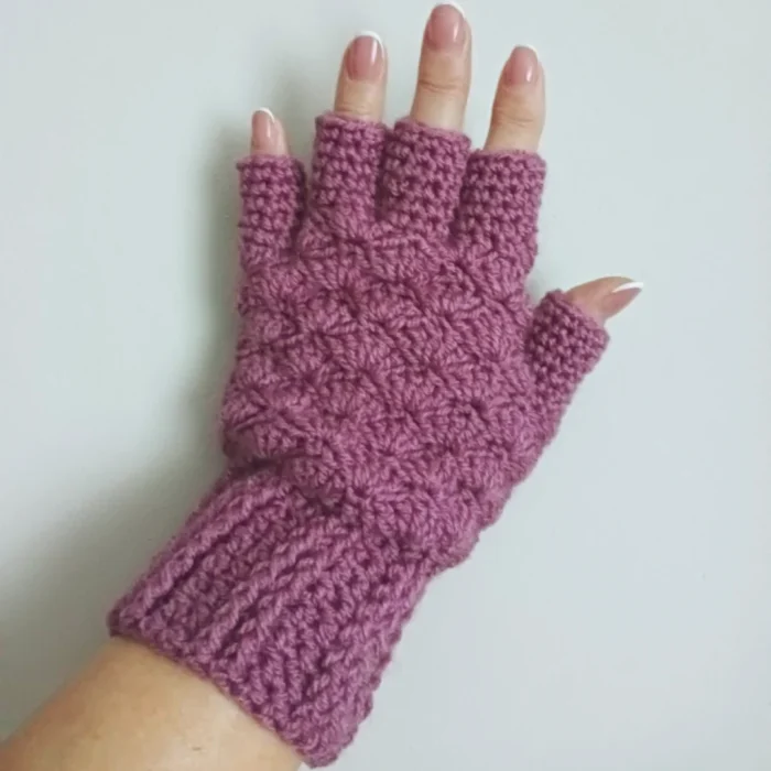 Zimowe szydełkowe rękawiczki bez zakończeń palców zrobione z włóczki w kolorze liliowym, prezentowane na lewej dłoni.