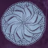 Serwetka-okragla_8 Biała, okrągła serwetka ręcznie robiona na drutach z bawełnianego kordonka. Posiada skomplikowany, mistery ażurowy wzór układający się w promieniującą rozetę lub spiralny wiatraczek, ułożona płasko na ciemnym, purpurowym tle o aksamitnej teksturze.
