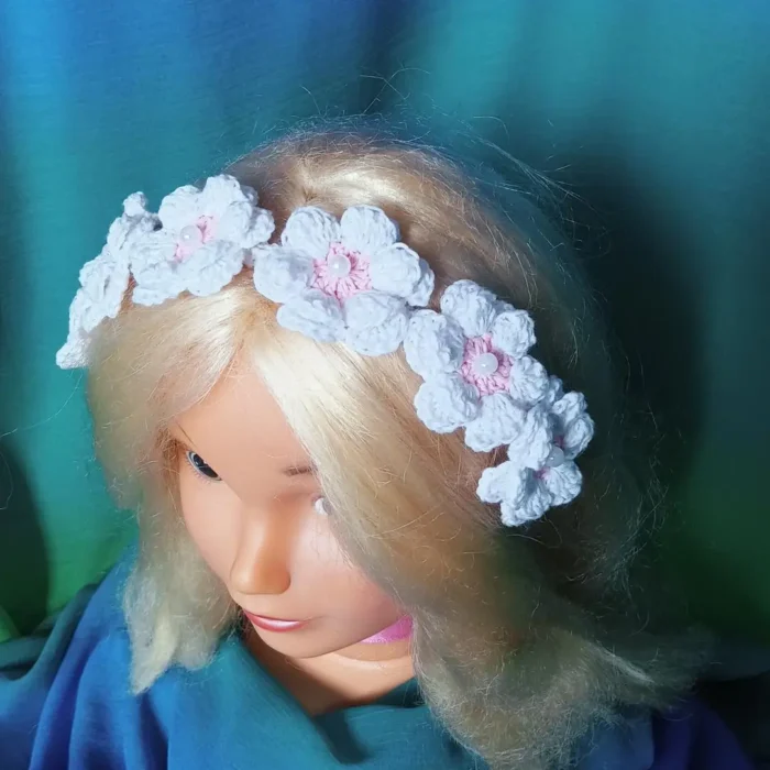 Szydełkowa opaska dla dziewczynki na białej, bawełnianej bazie, ozdobiona siedmioma trójwymiarowymi kwiatami z perłami.