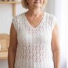 Biała ażurowa bluzka handmade z dekoltem w serek, ręcznie dziergana na drutach, prezentowana na sylwetce dojrzałej kobiety w jasnym wnętrzu.