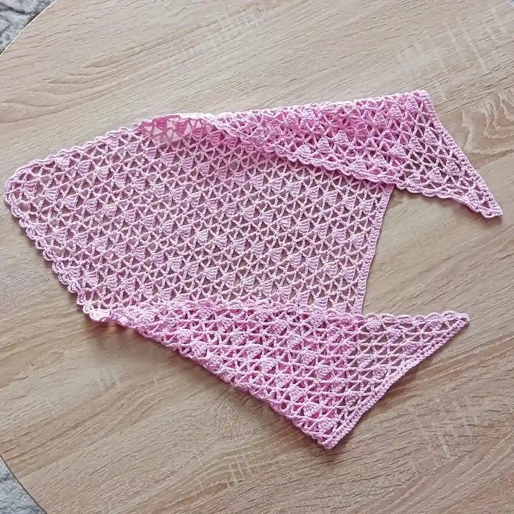 łożona różowa szydełkowa bandana na drewnianym stole.
