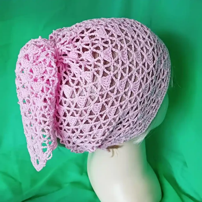 Chustka bandana zrobiona na szydełku_7 Tył głowy manekina w różowej szydełkowej chustce z węzłem, na zielonym tle.