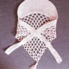Trójkątna chustka z daszkiem zrobiona na szydełku w odcieniu brudnego różu, ułożona na płasko. Dokładnie widać siateczkowy wzór rękodzieła, długie troczki do wiązania oraz ozdobny chwost na samym dole.